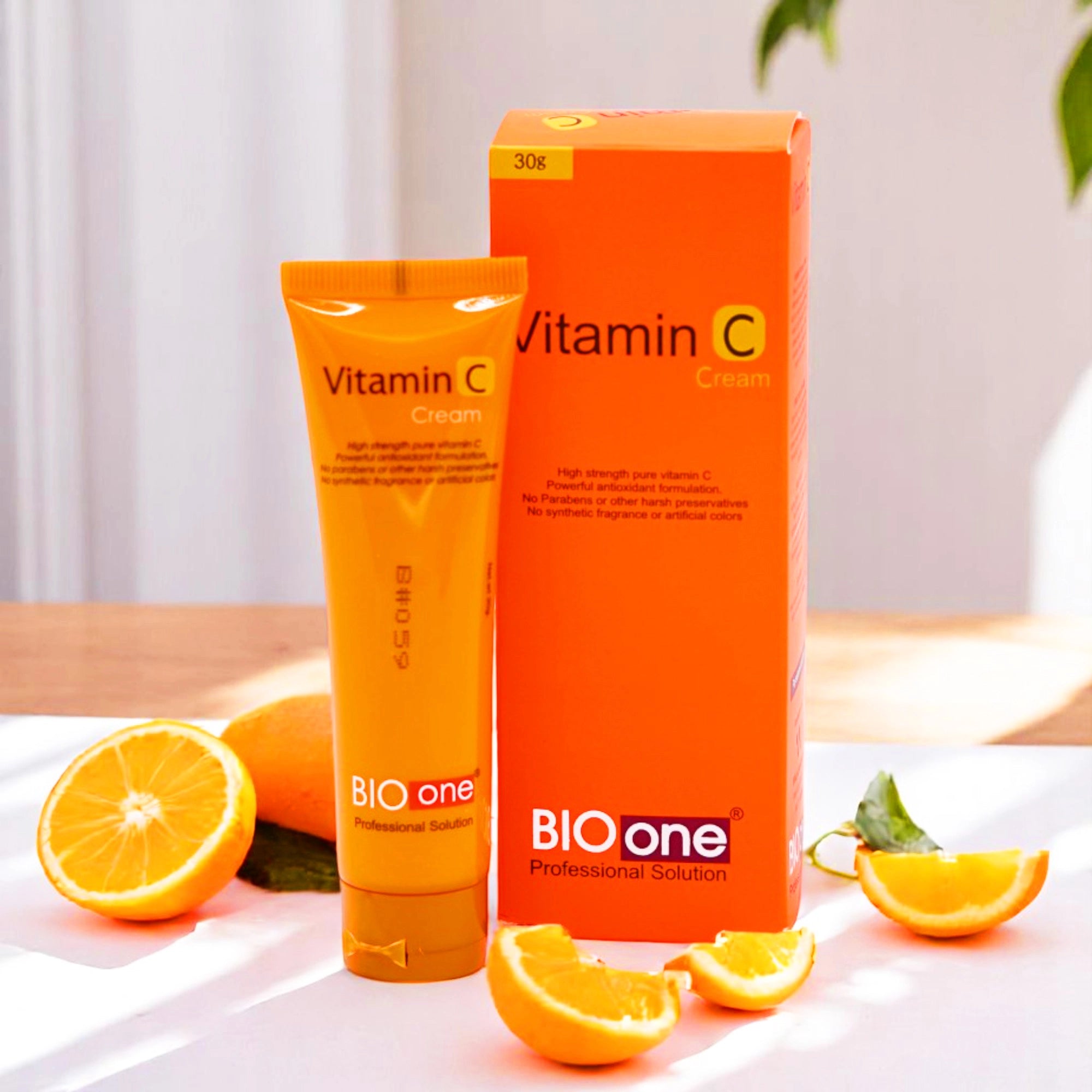Bio One Vitamin C Cream, 30g orange tube and its matching orange box, surrounded by sliced oranges.