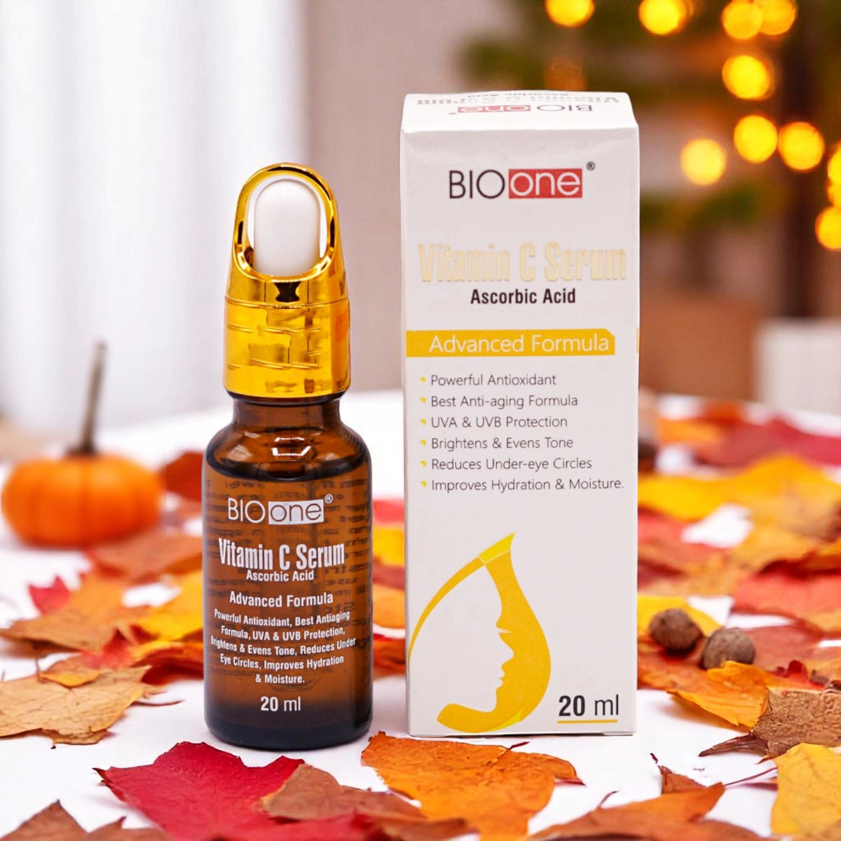Bio One Vitamin C Serum with Ascorbic Acid, 20ml amber dropper bottle with a gold top and a white and black label, alongside its white and gold box, set against an autumn-themed background with colorful leaves and a small pumpkin.