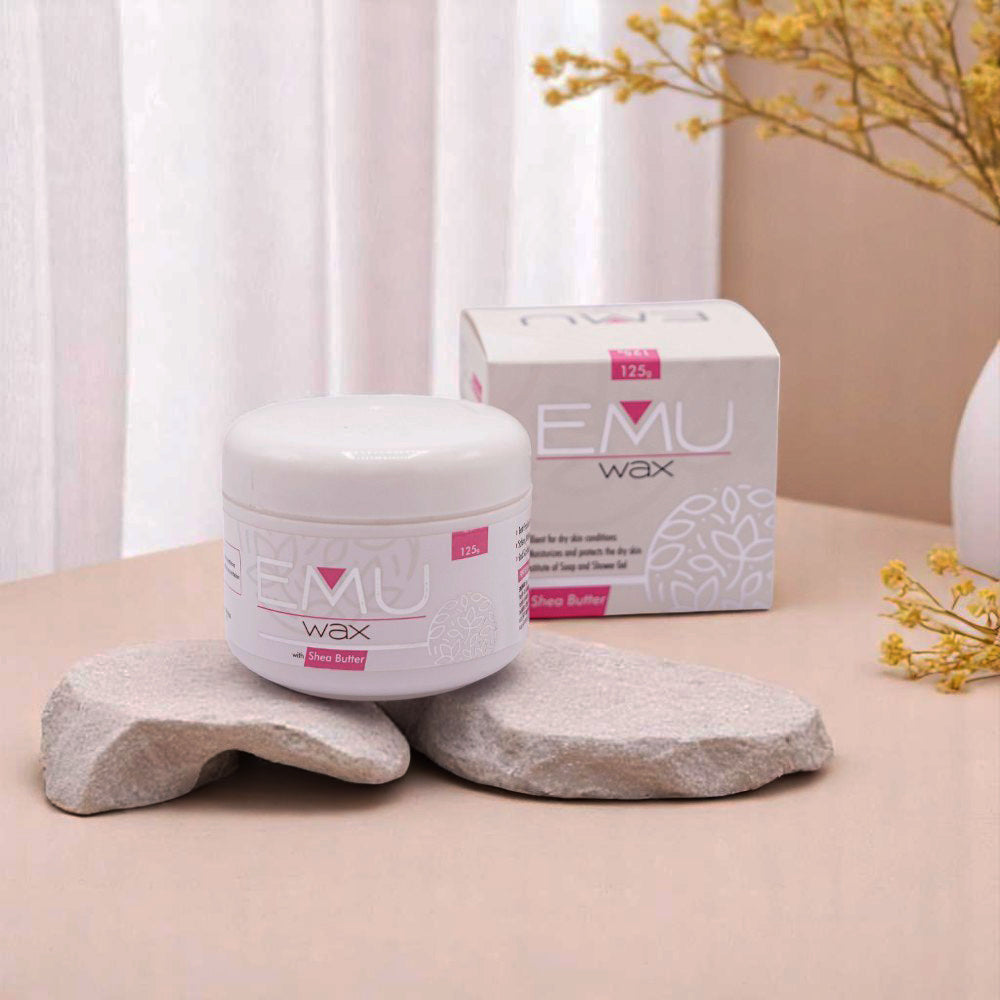 Emu Wax in a white jar with a pink label and its matching white and pink box, set on two light-colored, rough-hewn stones, with yellow flowers in the background.