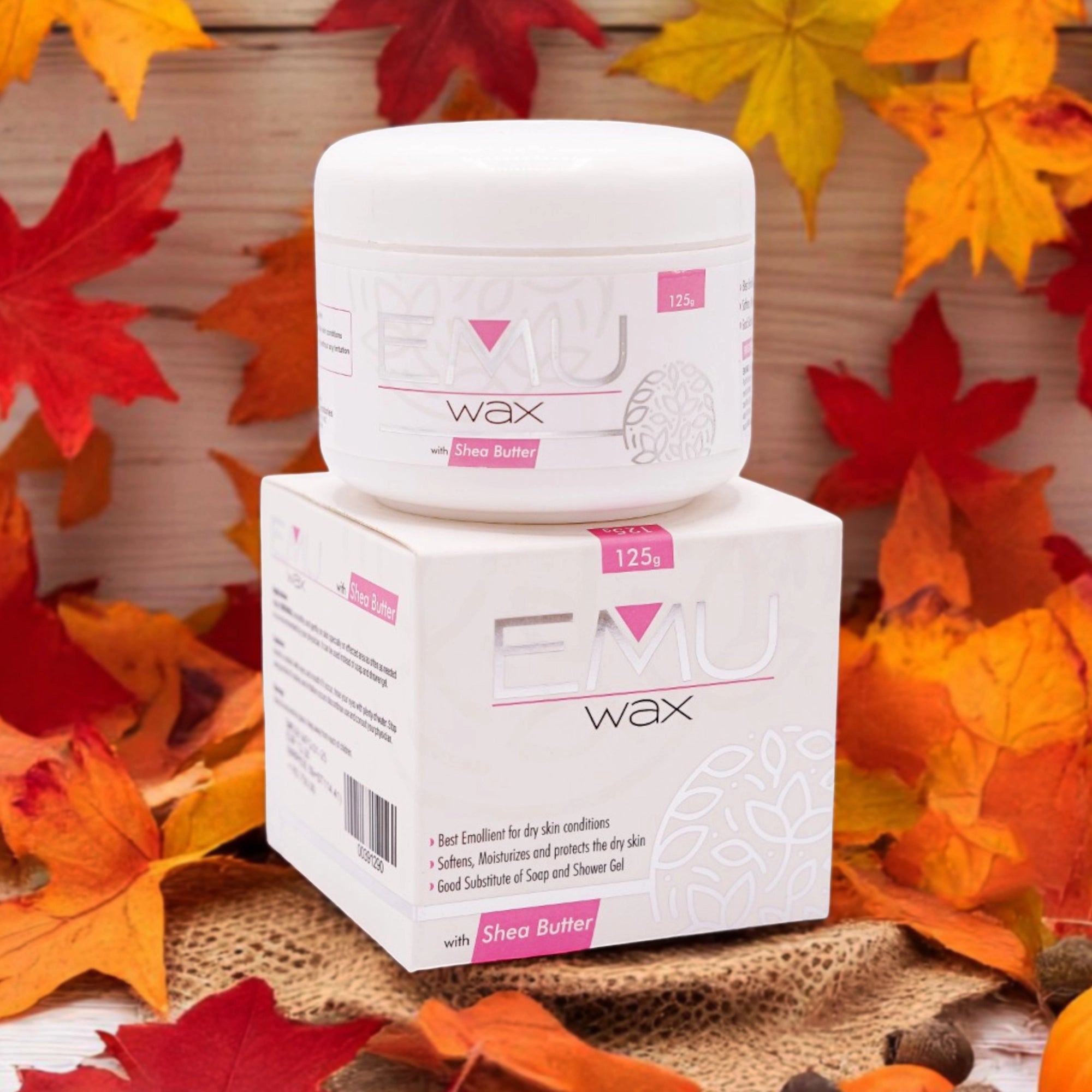 Emu Wax with Shea Butter, 125g white jar with a pink label, and its matching white box, set against a background of colorful autumn leaves.