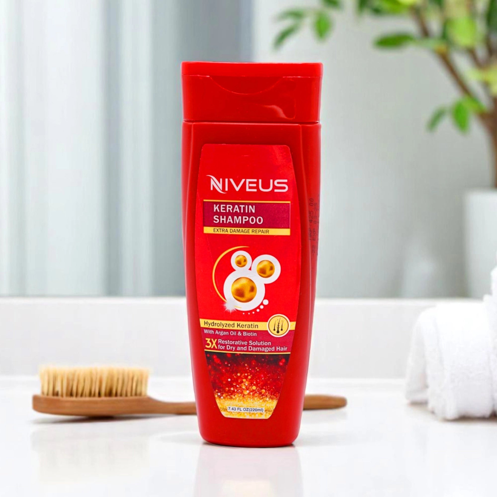 Niveus Keratin Shampoo, red bottle with a red flip-top cap, and its matching red box, set on a bathroom counter with a wooden hairbrush and white towels in the background.