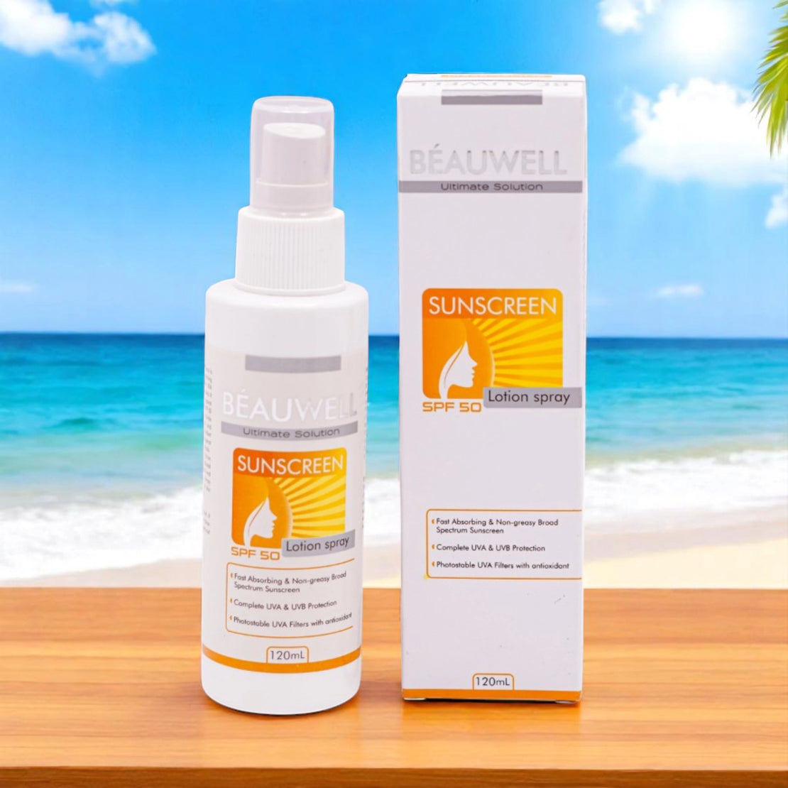 Beauwell Ultimate Solution Sunscreen Lotion Spray SPF 50, 120ml white spray bottle with a yellow and orange label, and its matching white and yellow box, set on a wooden surface with a blurred beach and ocean background.
