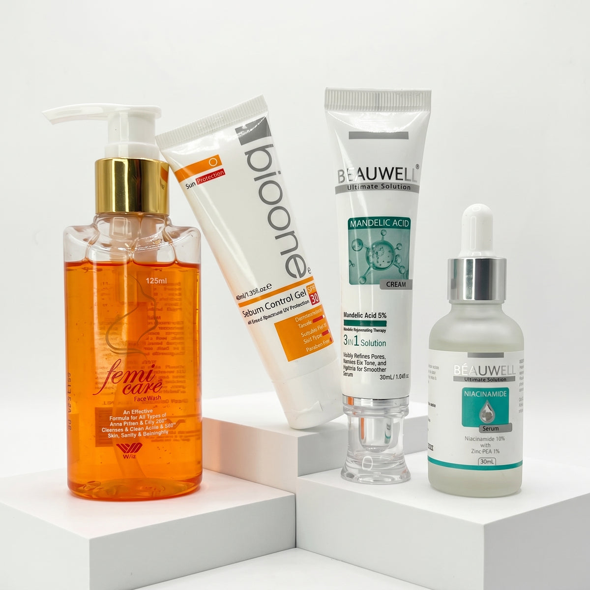 Whiz Clear Skin Kit featuring Femicare cleanser, Bio One Sebum Control Gel, Beauwell Mandelic Acid 5% serum, and Beauwell Niacinamide 10% serum on white pedestal blocks.