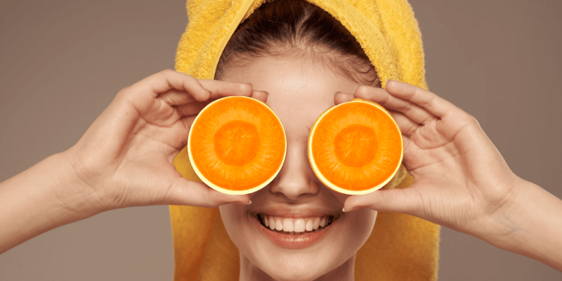 cheerful woman holding carrots near her eyes skincare