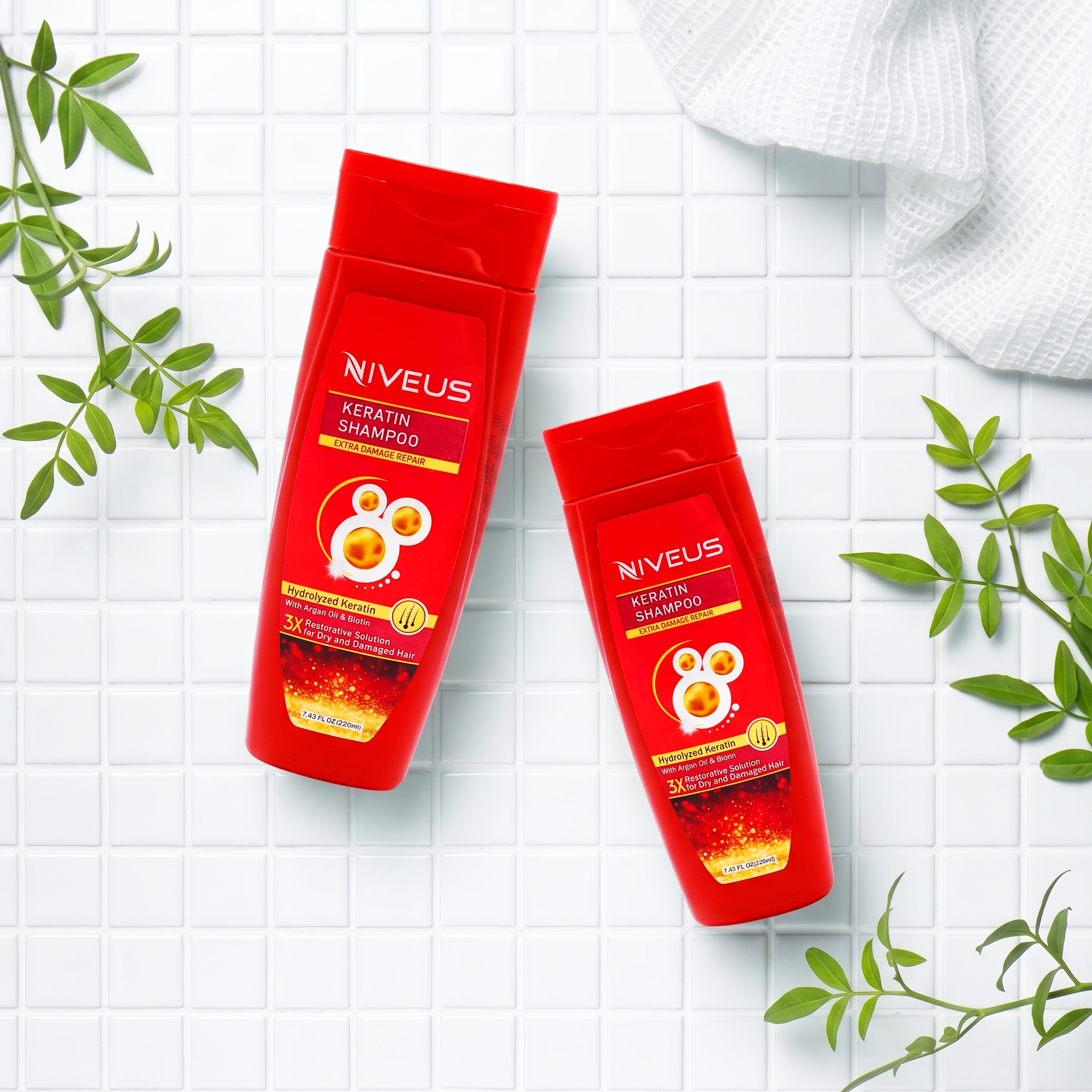 Two red bottles of Niveus Keratin Shampoo for extra damaged hair on a white tiled surface with green leaves